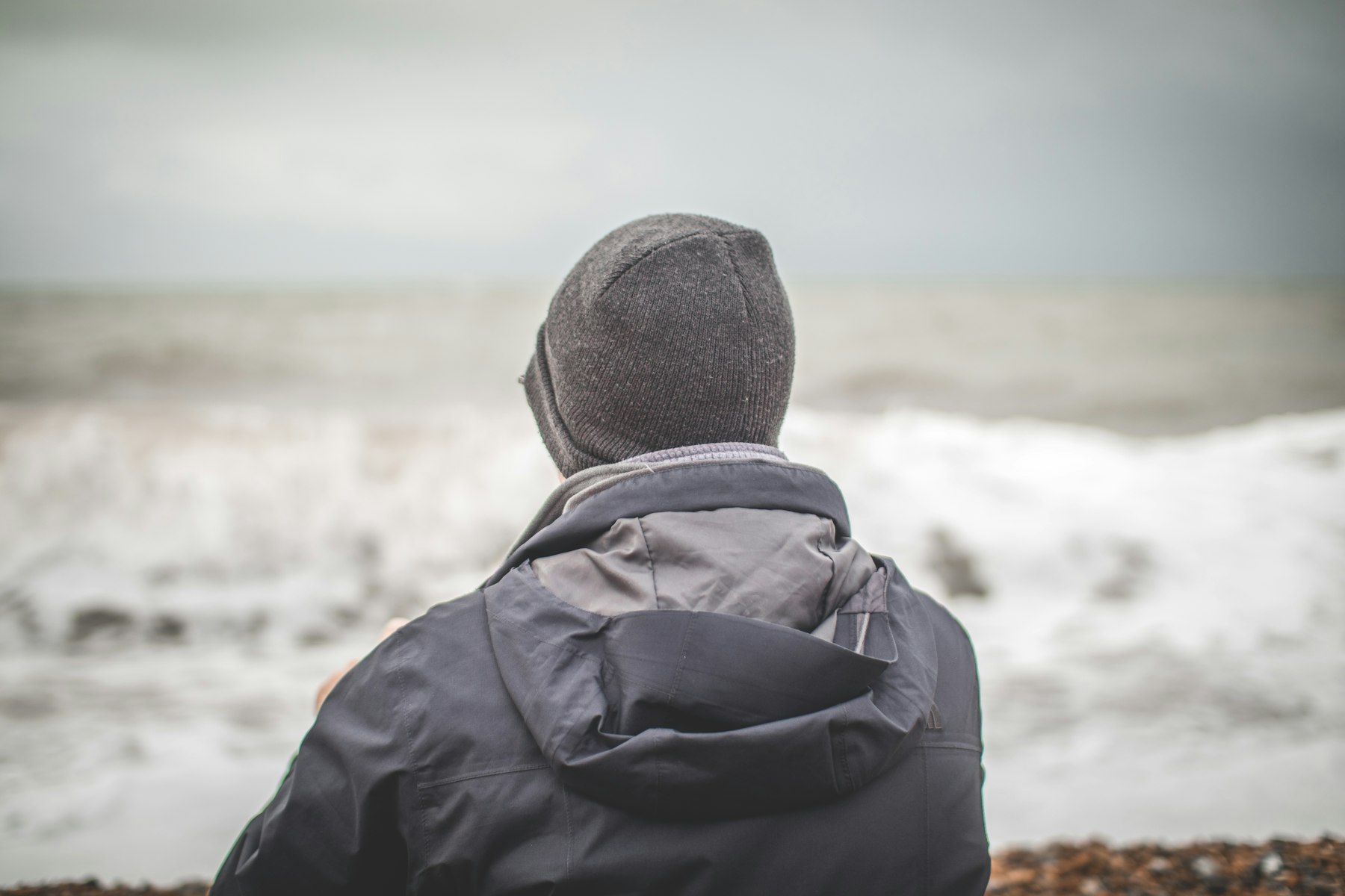A man in a hood looks out at a rough sea